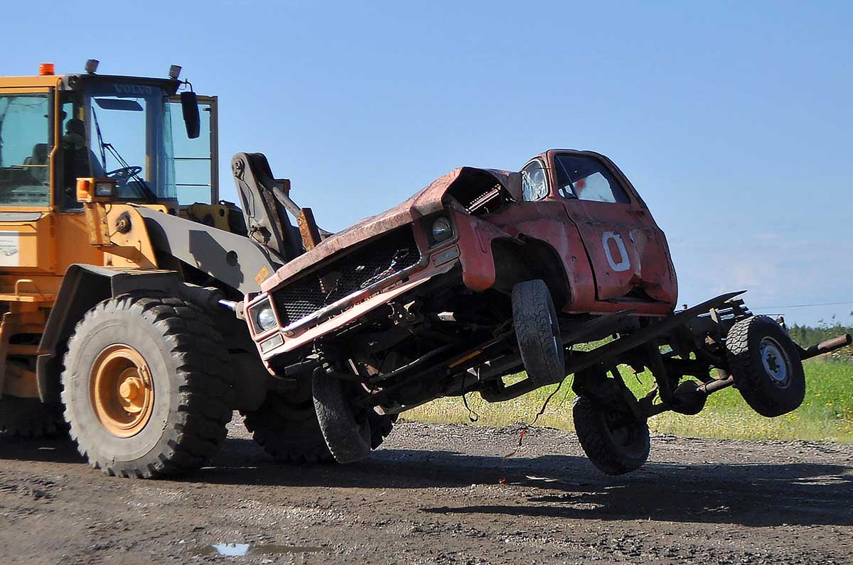 A contractor uses a forklift to pick up a junked truck