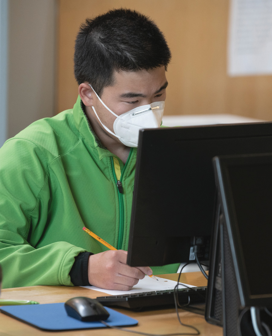 student wearing mask writing something down in front of his computer