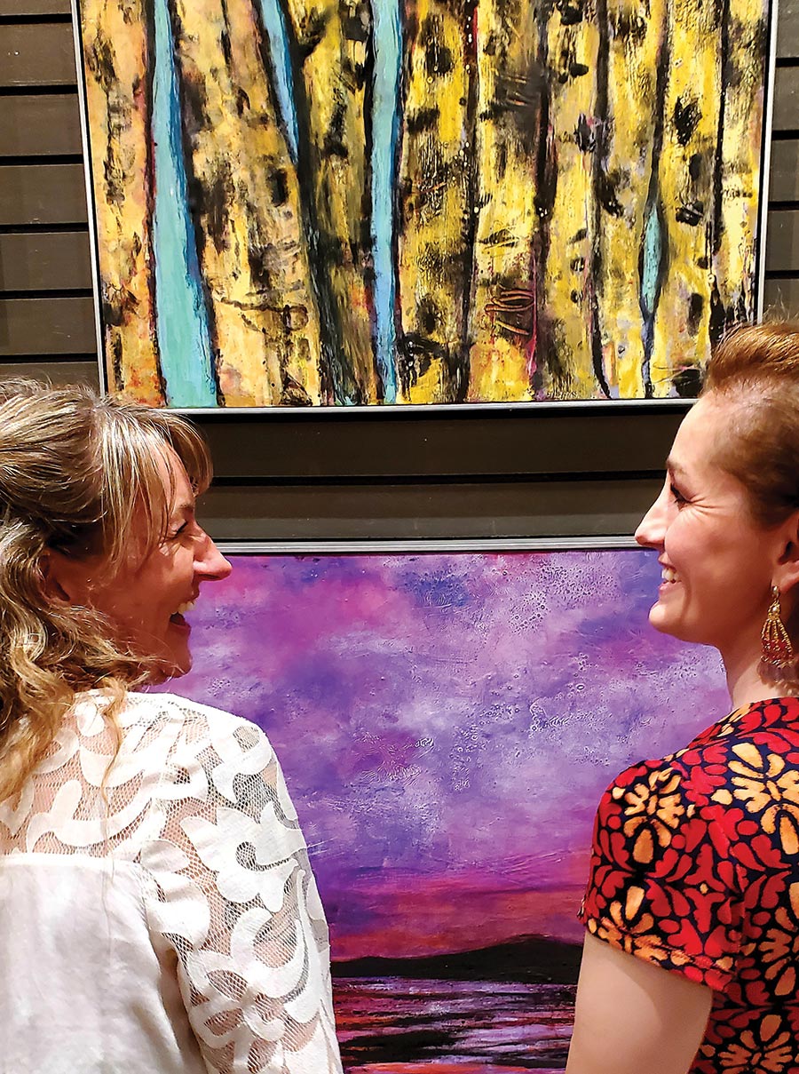 Stephan Fine Arts owner Becky Stephan (right) explaining her painting technique to Dos Manos co-owner Kara Kirkpatrick at a First Friday event in May