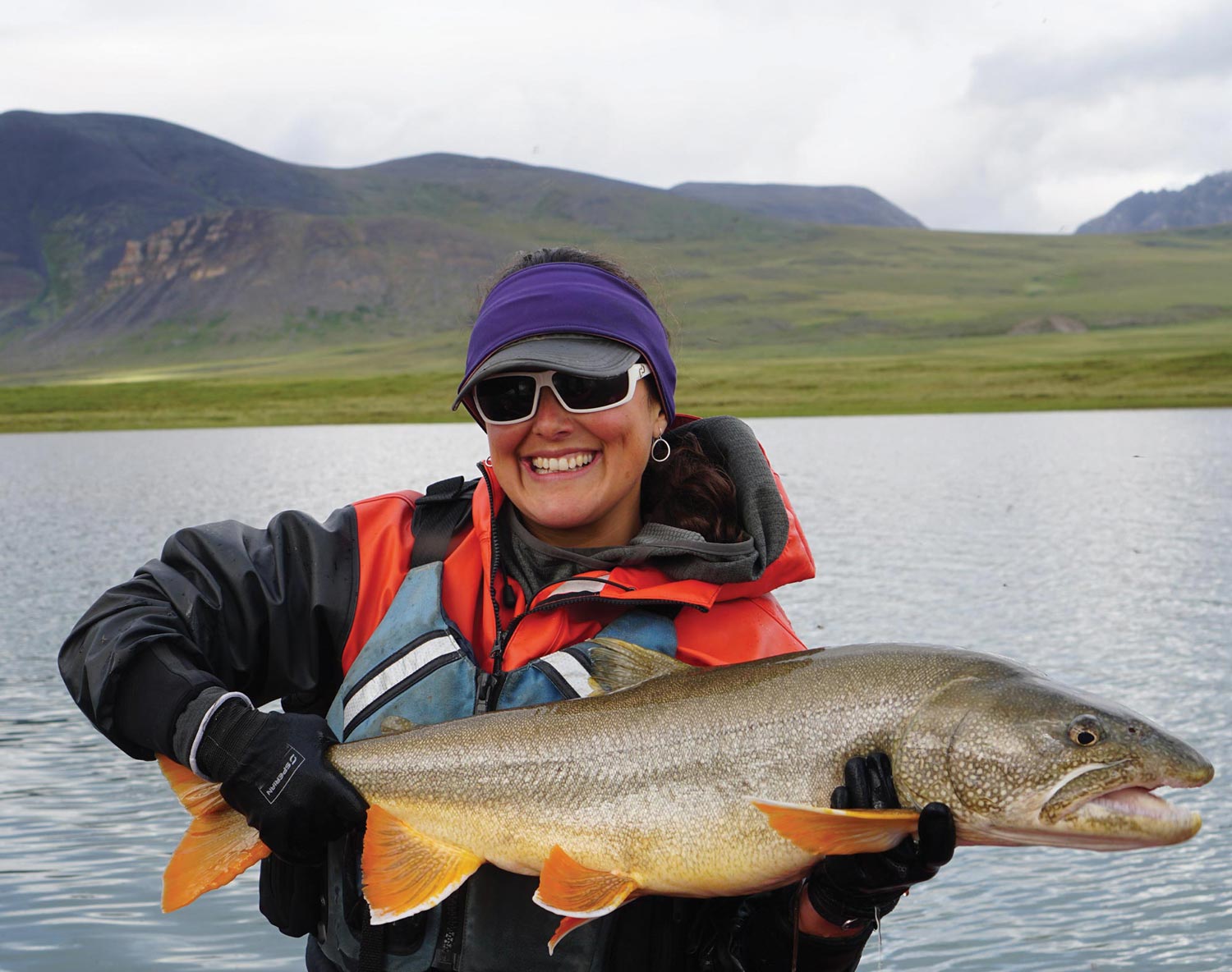 a woman smiles holding a large fish while in the middle of a body of water