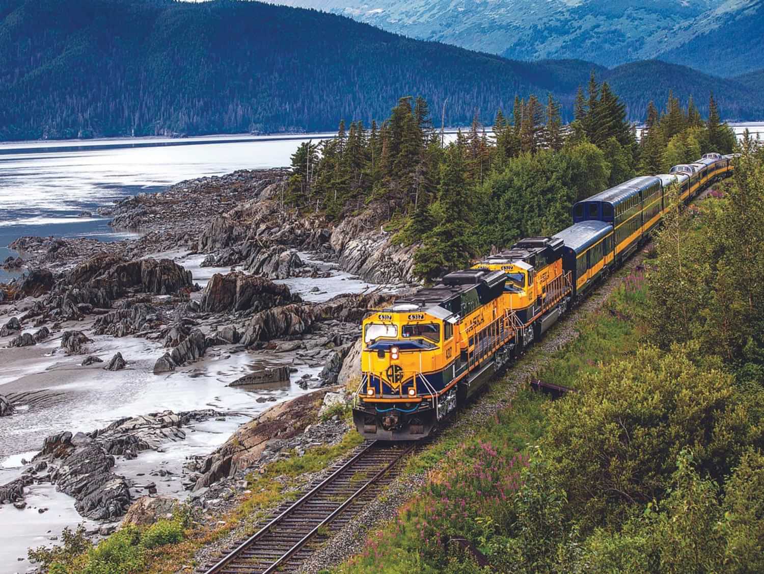 an Alaska Railroad train travels tracks by a body of water