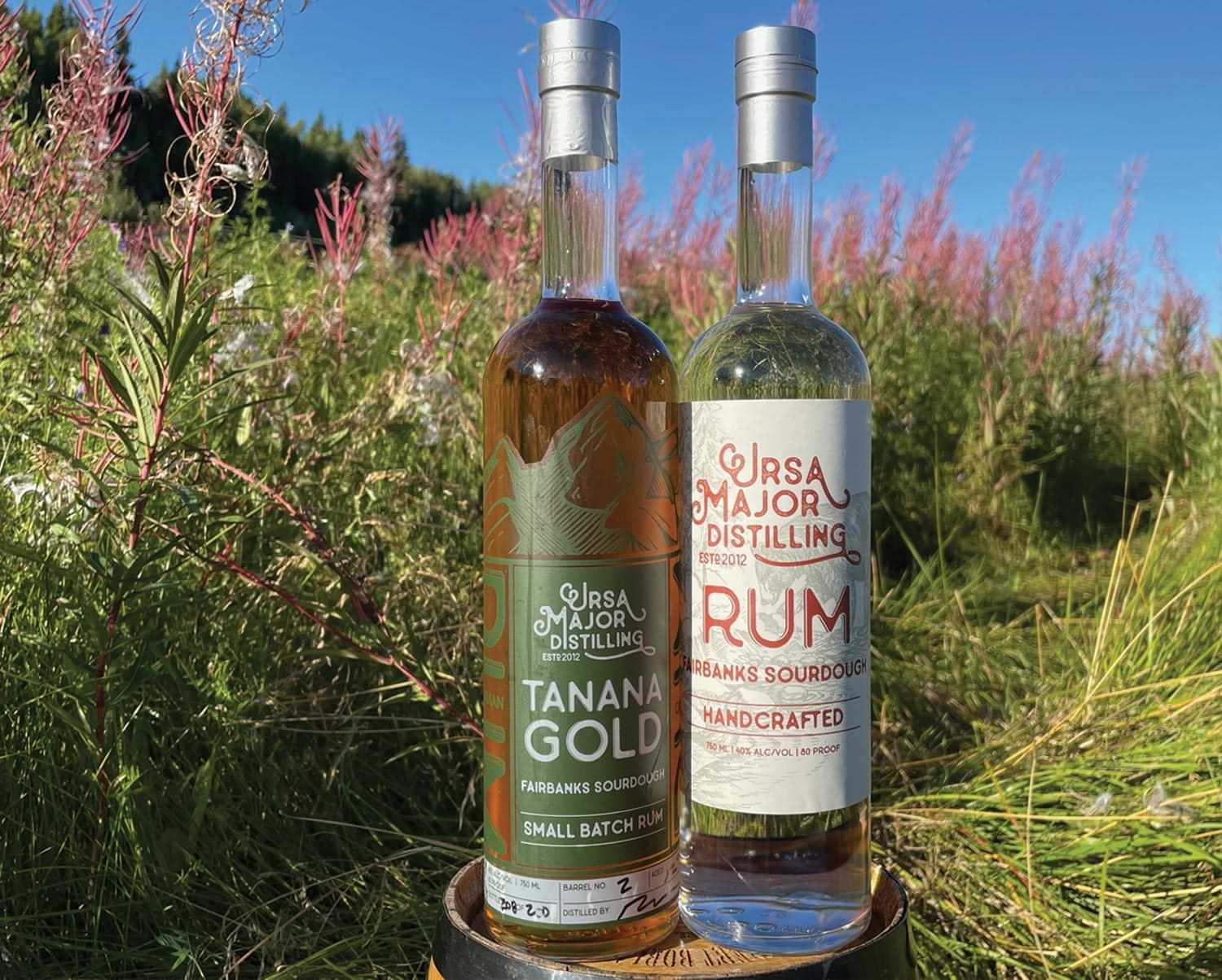 two bottles of rum from Ursa Major Distilling sit on a barrel among shrubs