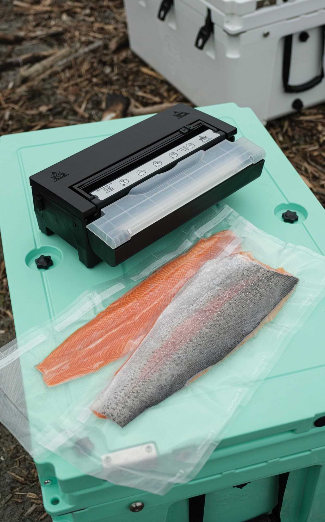 a PacBak vacuum sealer sits on a mobile cooler next to two vacuum sealed salmon fillets