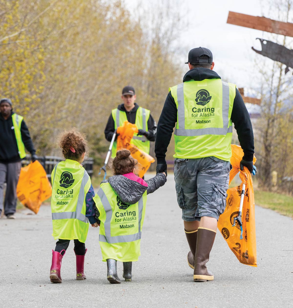 two kids and an adult with "caring for alaska" vests on