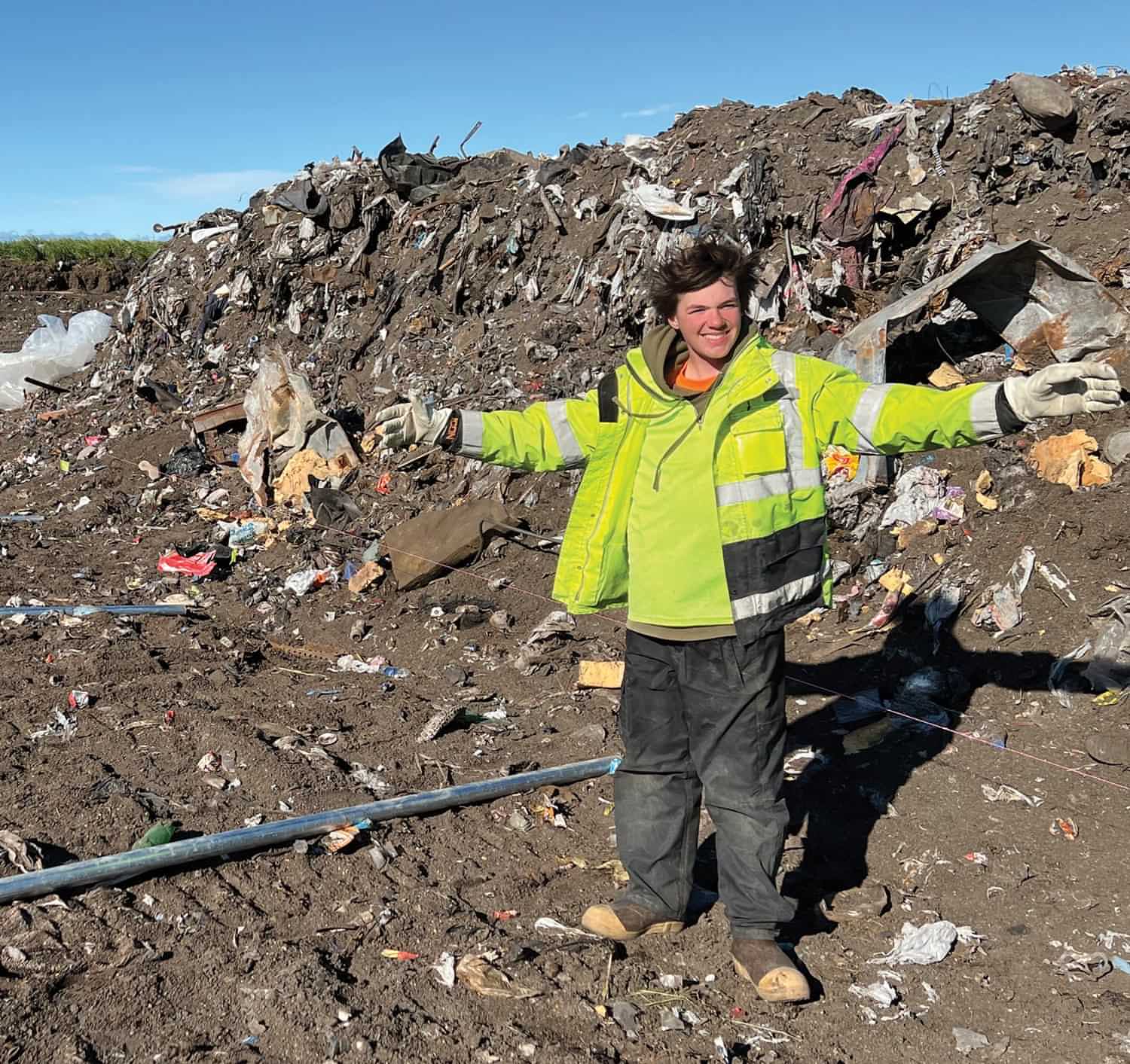 a man stands at the Kivalina Landfill with arms outstretched for a picture