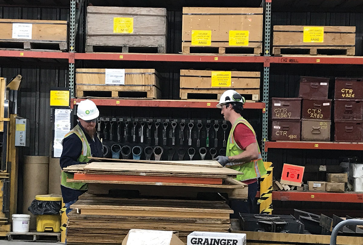 Two workers in hard hats and neon vest measuring some plywood