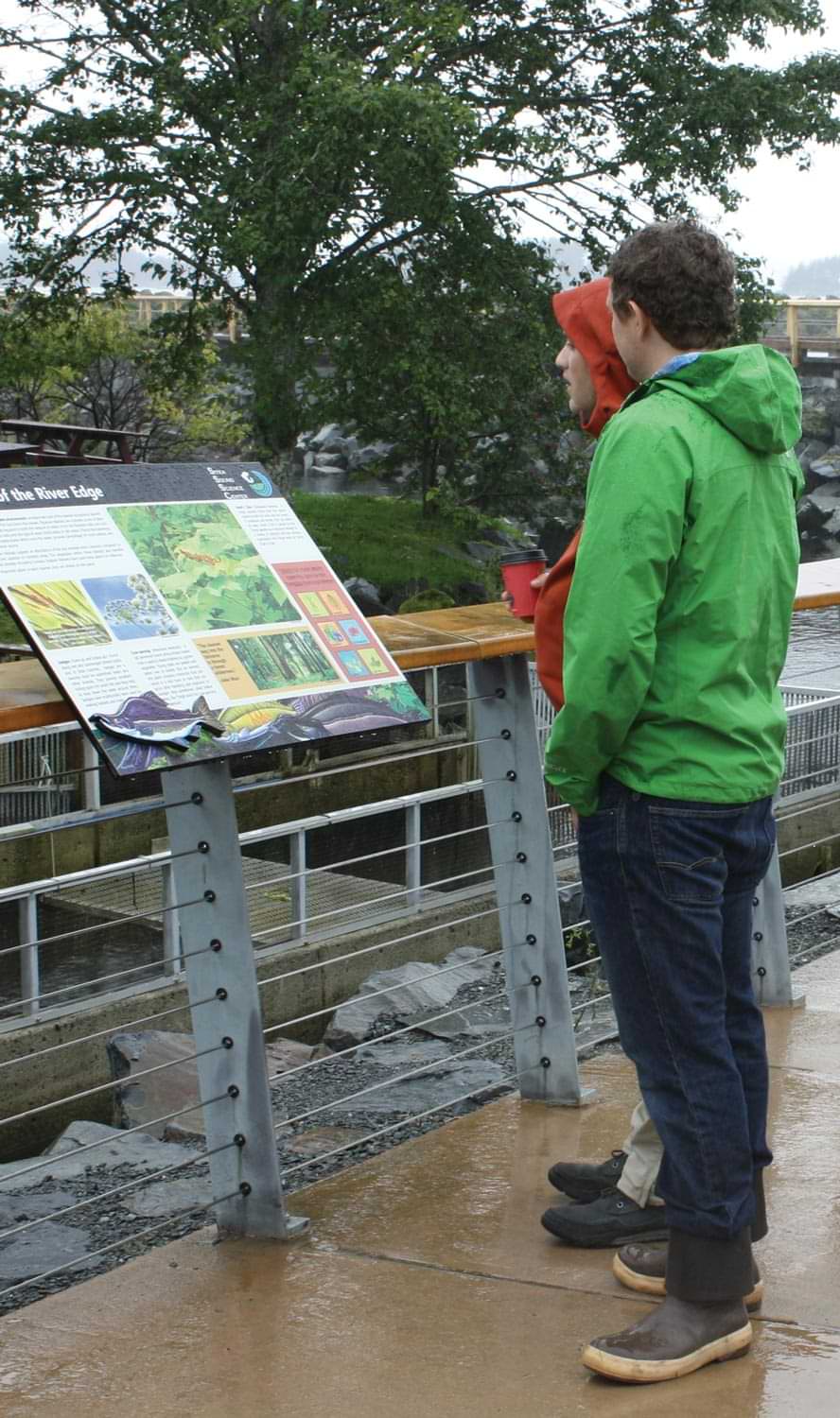 a man and woman stand outside looking at a habitat information sign