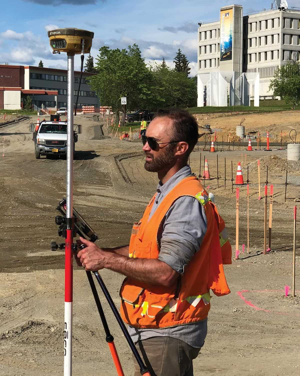 a man in a safety vest stands at a construction site holding a tripod mounted device
