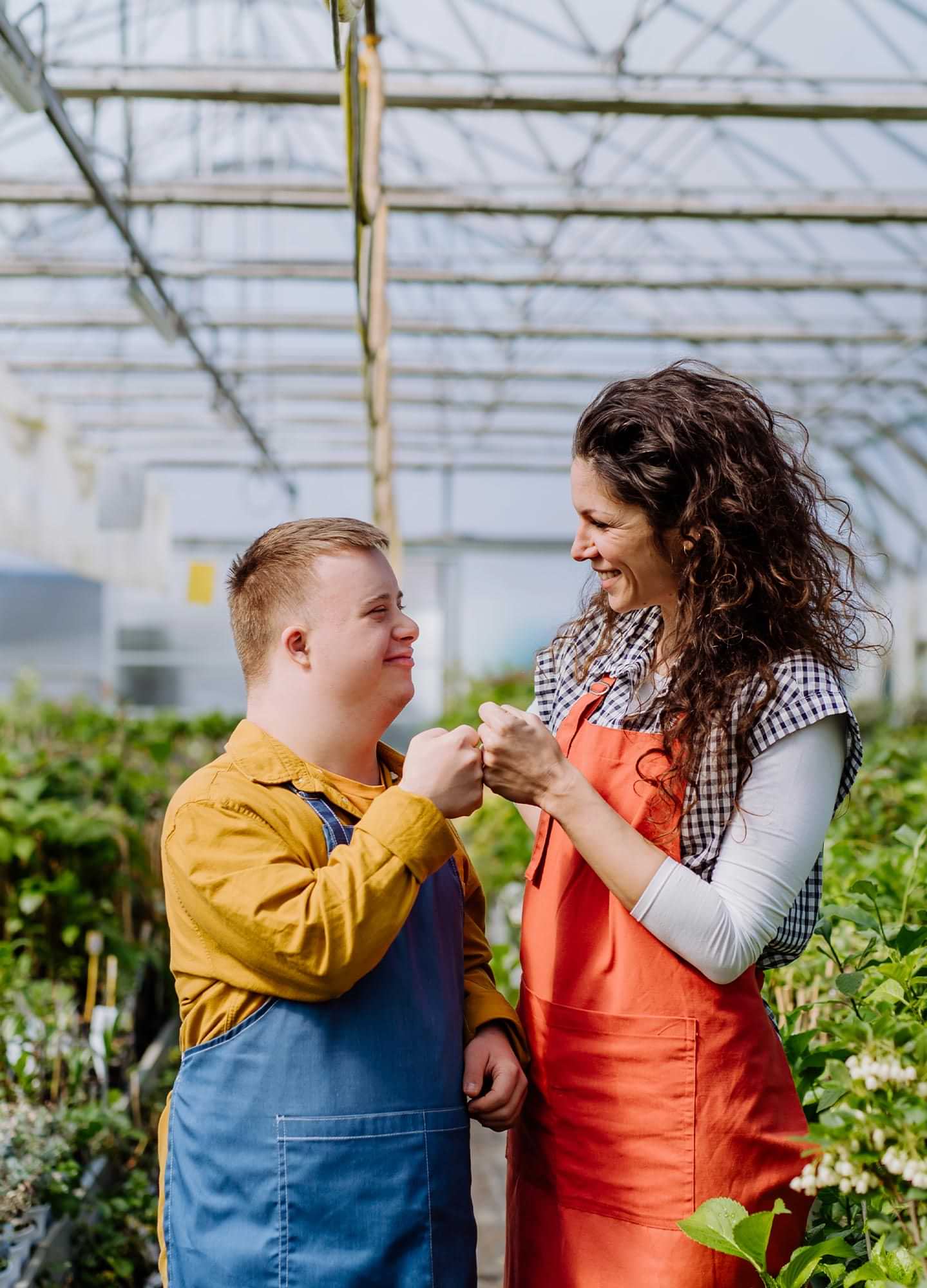 a women and young man smile while fist bumping in a full green house