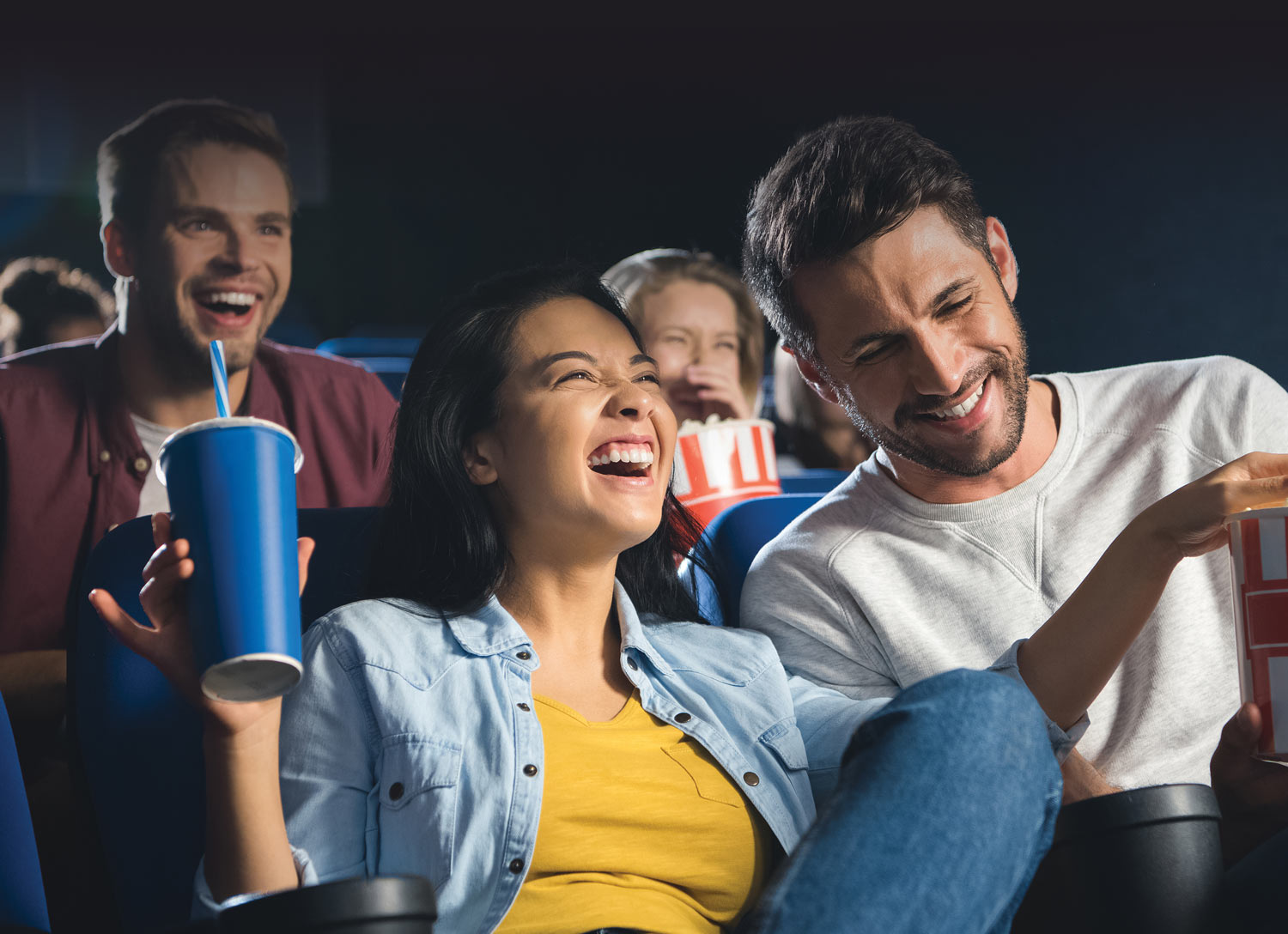 people laughing in a movie theater with popcorn and drinks
