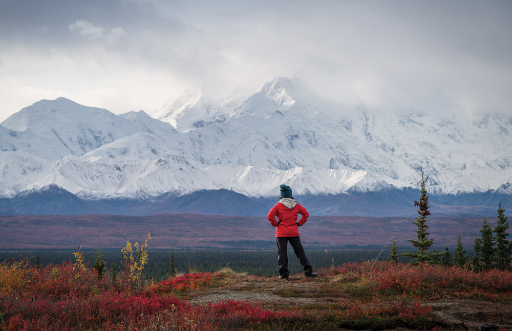 women in red jacket looking at mountain scape covered in snow