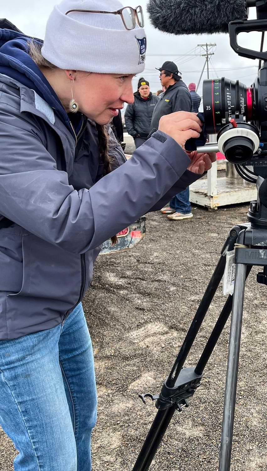 a woman looks closely as she cleans the lens of a highend camcorder on a tripod at the North Slope Marketplace
