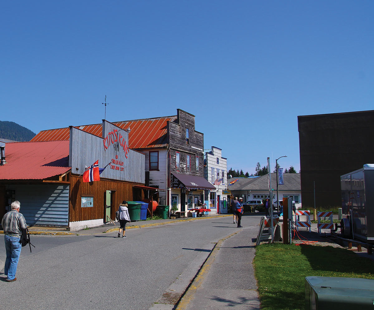 Portrait photograph of a street with buildings and people walking around within a cannery and sawmill area near a Tlingit fish camp on Mitkof Island during the day