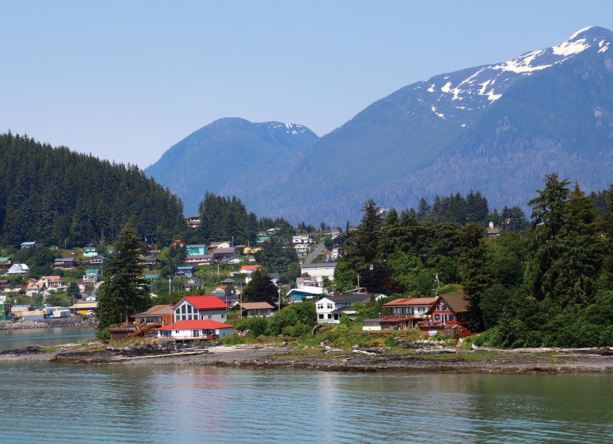 Landscape photograph of a small town with many green trees surrounding the area and mountains in the background situated nearby at the mouth of the Stikine River during the day