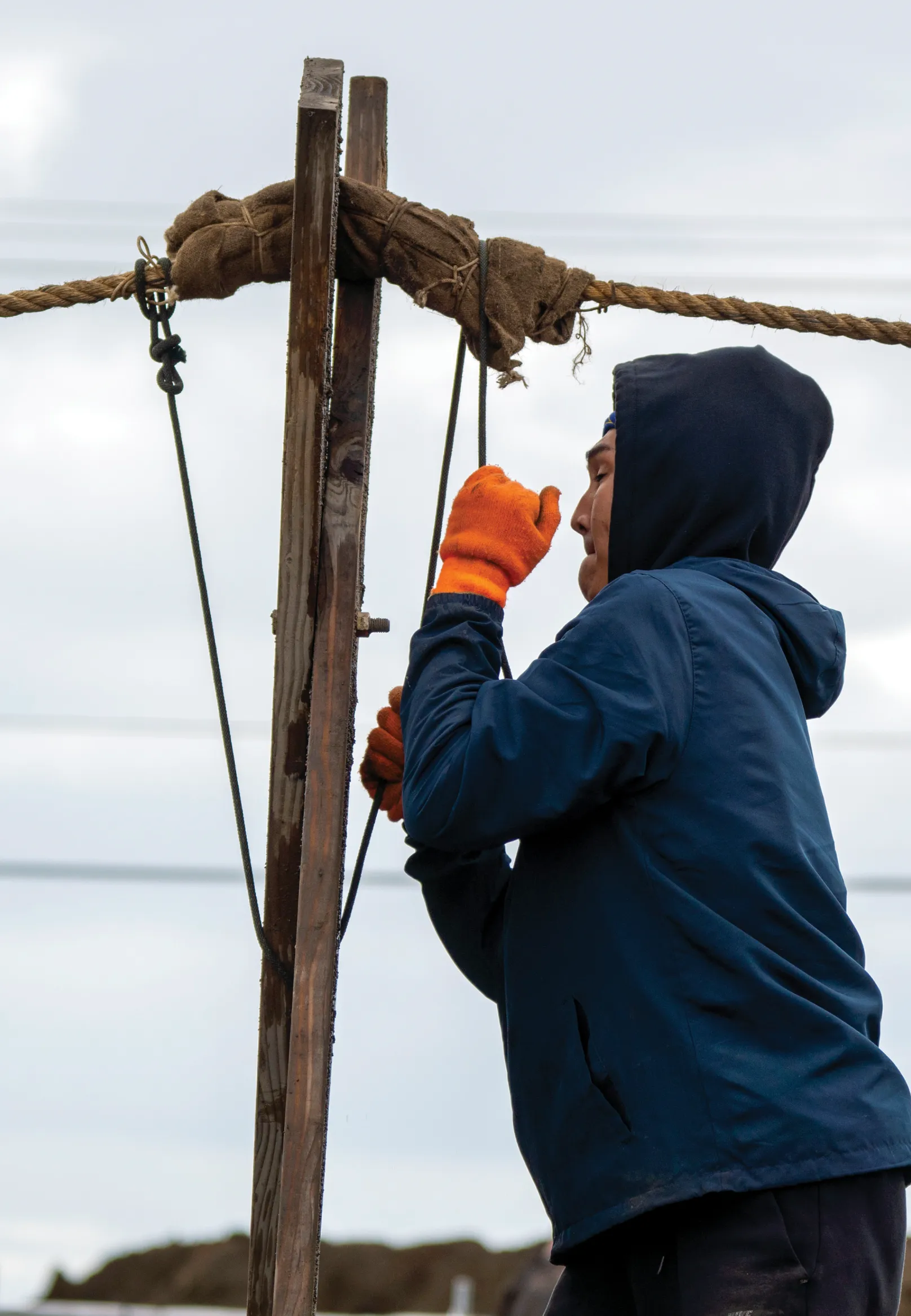 Man with orange gloves tightening rope around pole