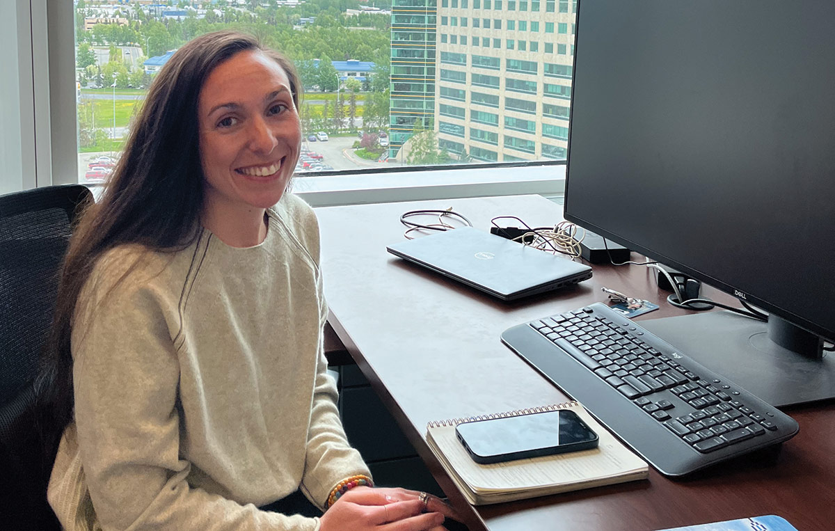 Landscape photograph of Mary Miner smiling from her office desk at McKinley Alaska Growth Capital; She can see the company’s former owner, Arctic Slope Regional Corporation, where the North Slope Marketplace program was created for the benefit of its shareholders.