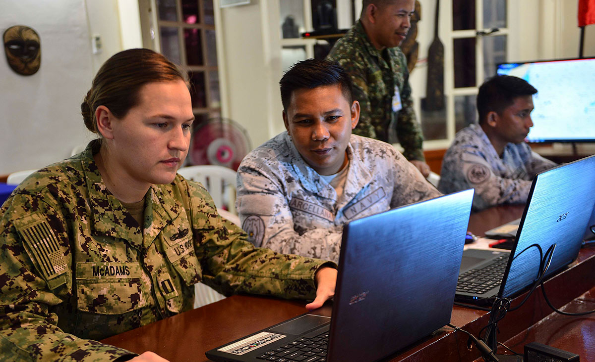 Close-up photograph perspective of officers of the US and Philippine navies using SeaVision on laptops to track vessels during a 2019 maritime partnership training activity