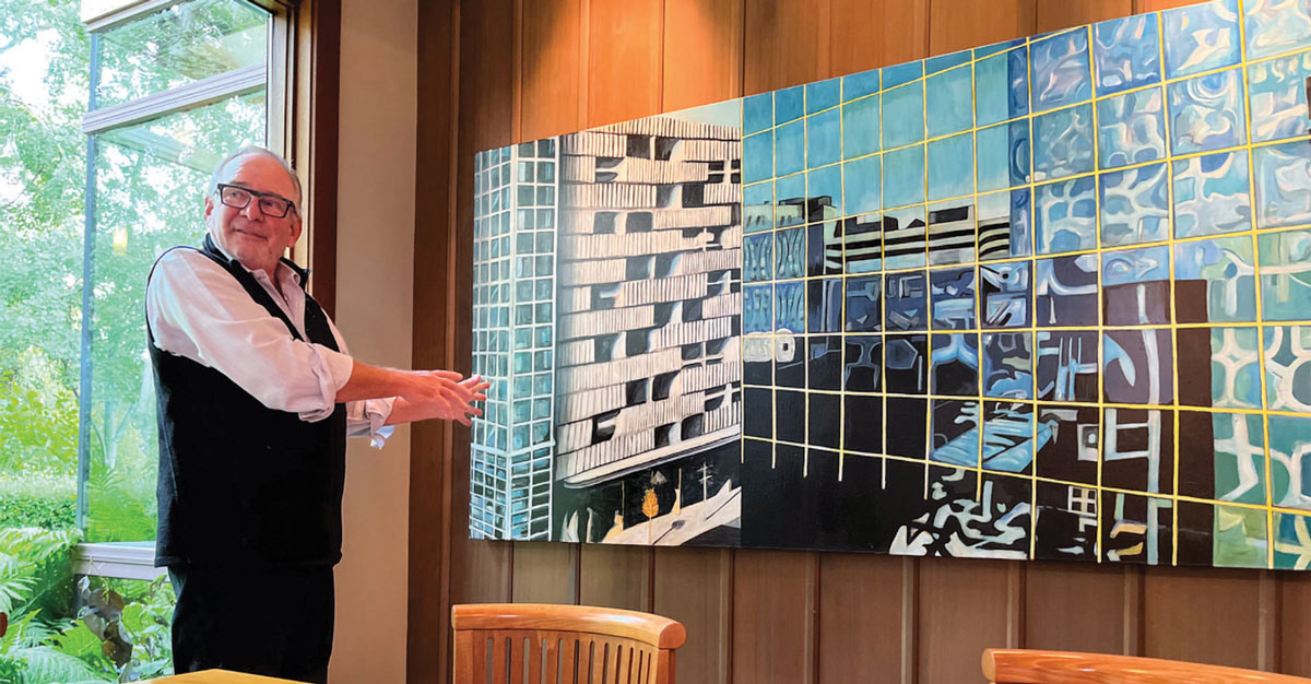 a man stands motioning to a large cityscape painting hanging on a dining room wall