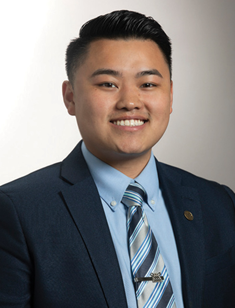 Headshot of a man wearing a dark blue suit jacket, blue shirt, and striped tie (Peng Thao)