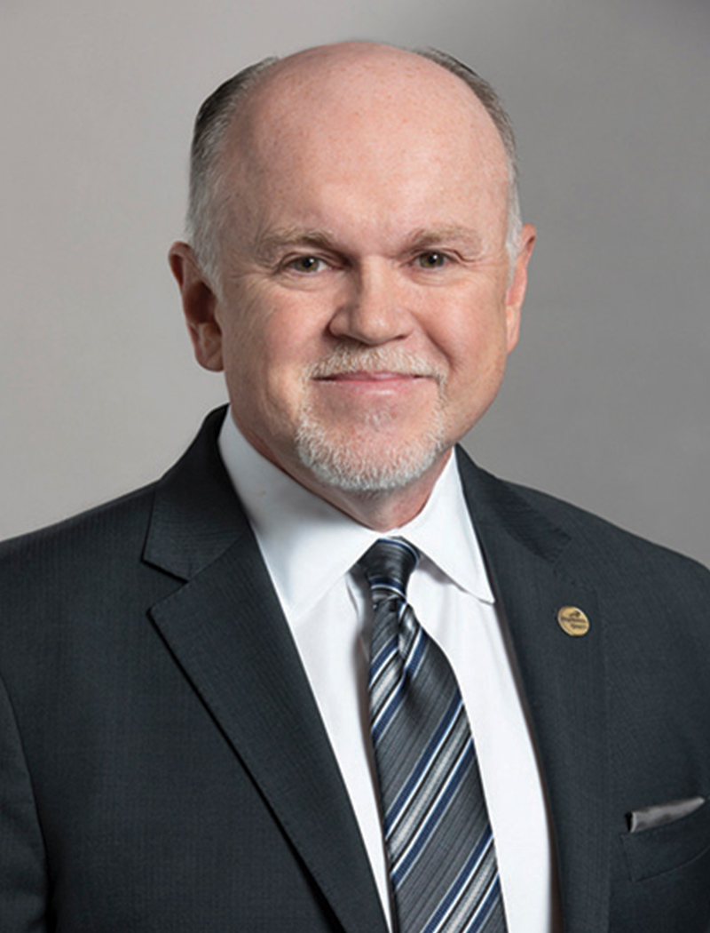 Headshot of a man wearing a black suit jacket, white shirt, and striped tie (Greg Deal)