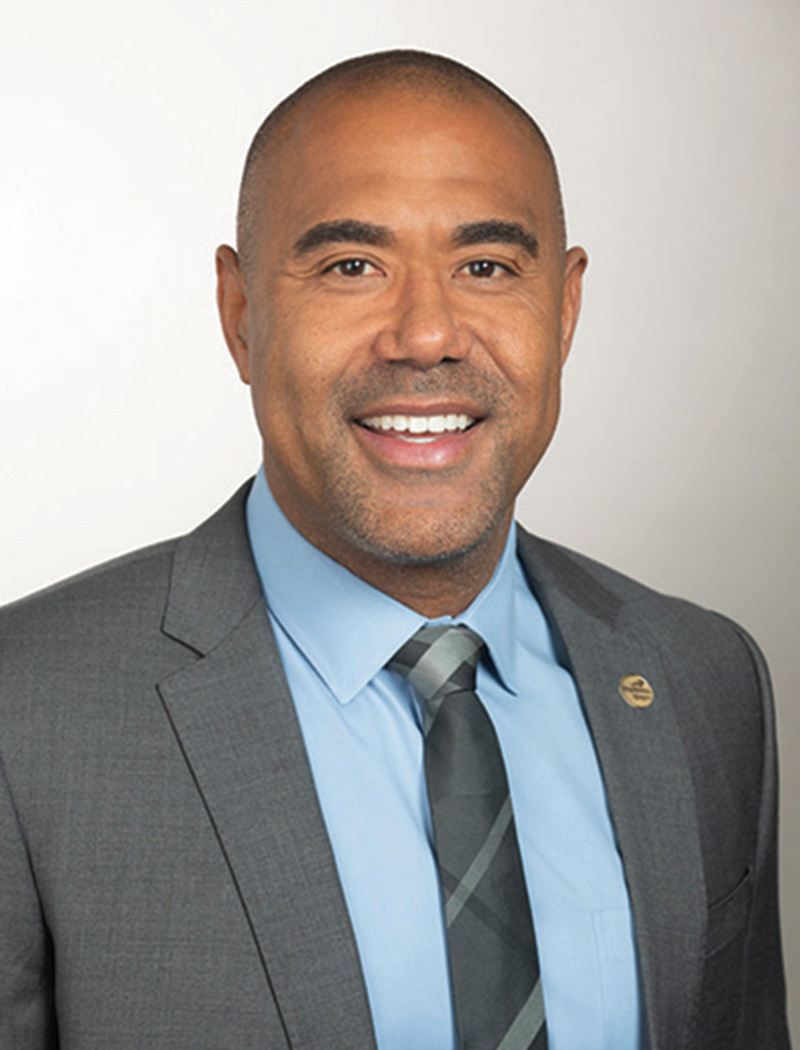 Headshot of a man wearing a gray suit jacket, blue shirt, and tie (Bill Bailey)
