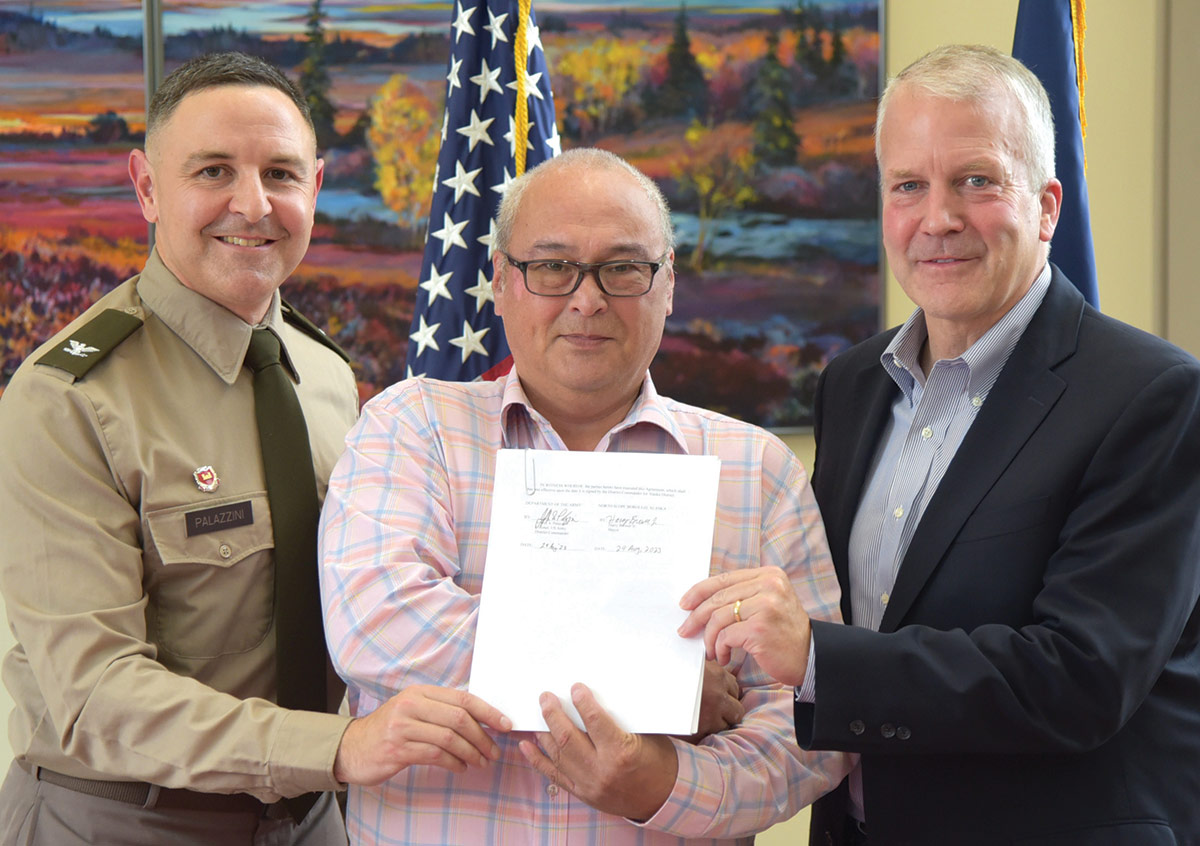 Close-up landscape photograph perspective of Colonel Jeffrey Palazzini, district commander, Harry Brower Jr., mayor of the North Slope Borough, and Senator Dan Sullivan posing next to each other for a picture as they all hold a white paper document with signatures on it; They participated in a ceremonial signing of the project partnership agreement for the Barrow Coastal Erosion Project in Utqiaġvik, Alaska.