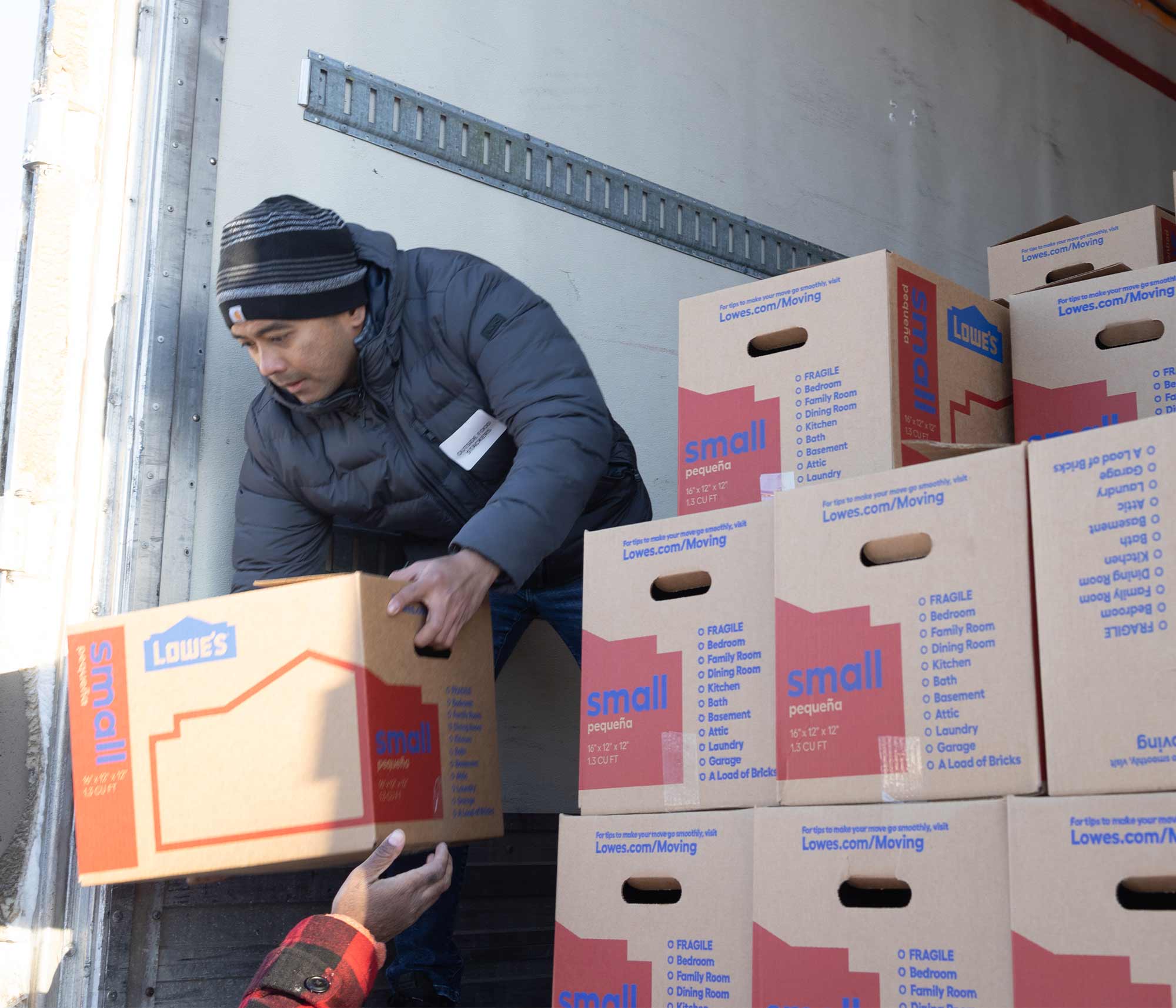 Man in beanie and winter jacket hoisting small boxes into a truck