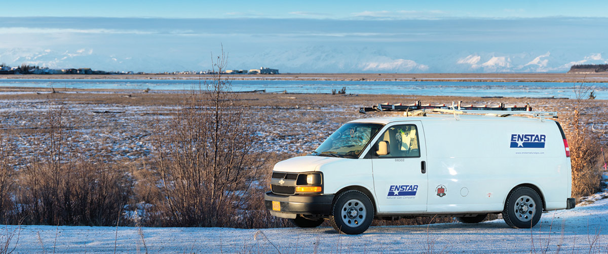 Landscape aerial photograph perspective of a white ENSTAR Natural Gas Company van parked on the snow ground near some scattered marsh during the day