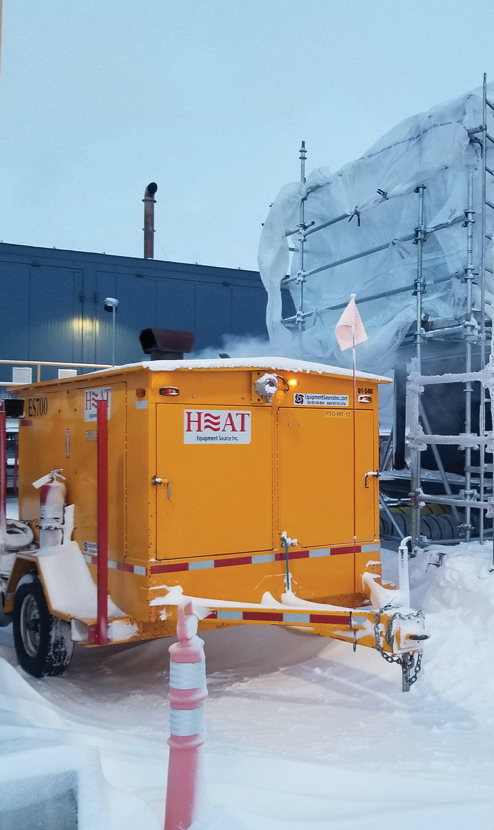 a large portable heating unit parked in the snow beside a large factory