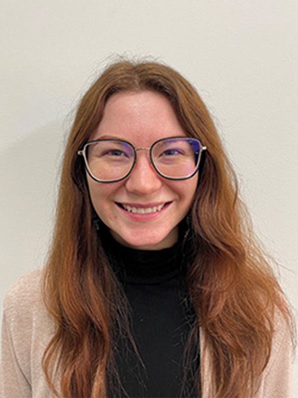 Headshot of a woman with long red hair, wearing glasses and a black shirt with a tan cardigan