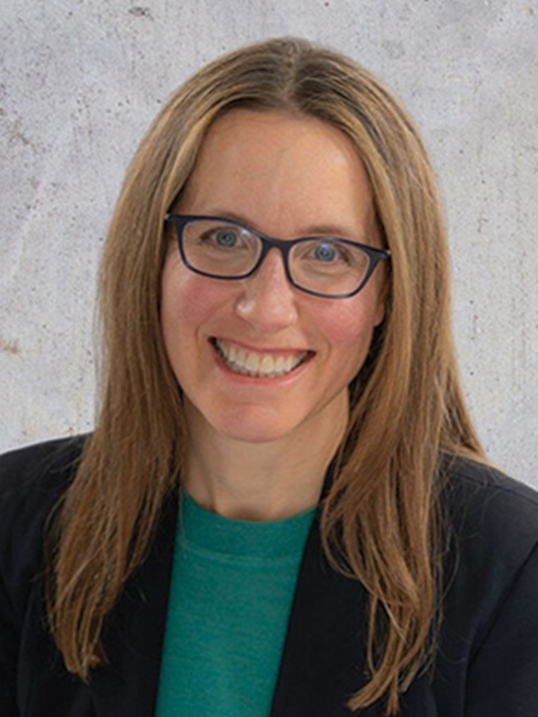 Headshot of a woman with medium blonde hair, wearing a black blazer over a green shirt