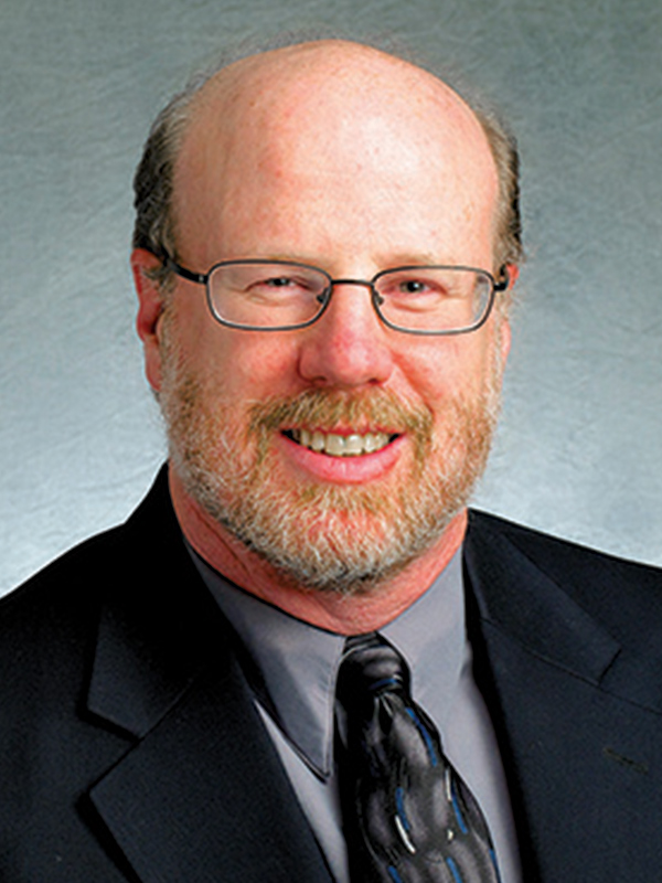 Headshot of a man wearing glasses and a suit and tie