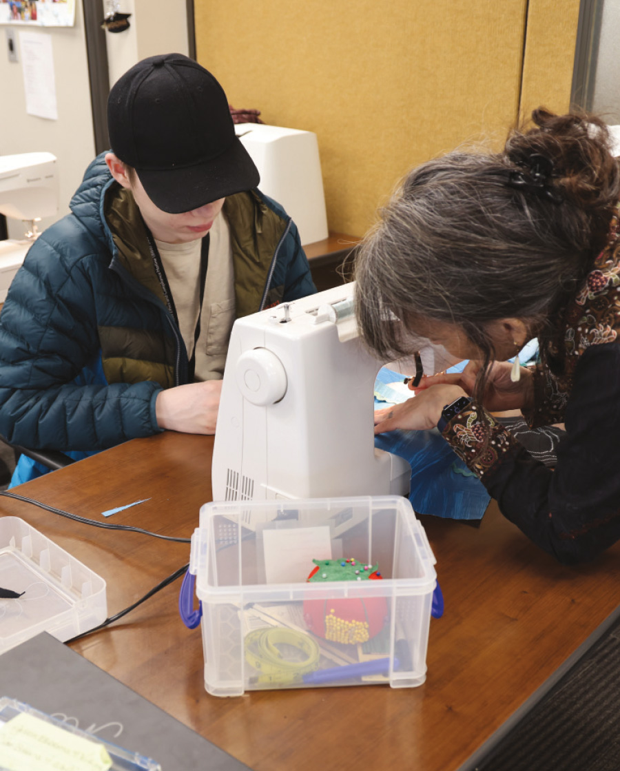 Woman showing young male a stitch on a sewing machine