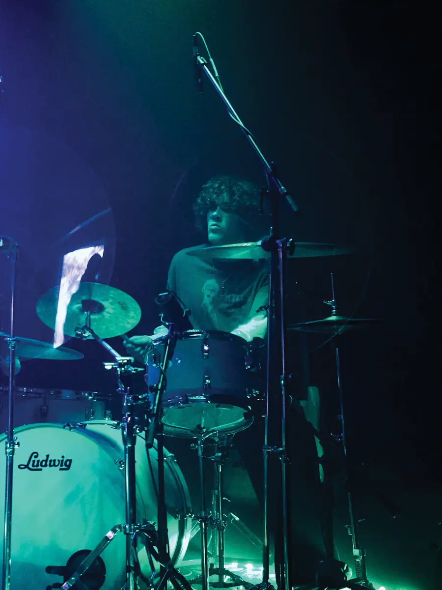 a drummer performing while illuminated by green stage lights