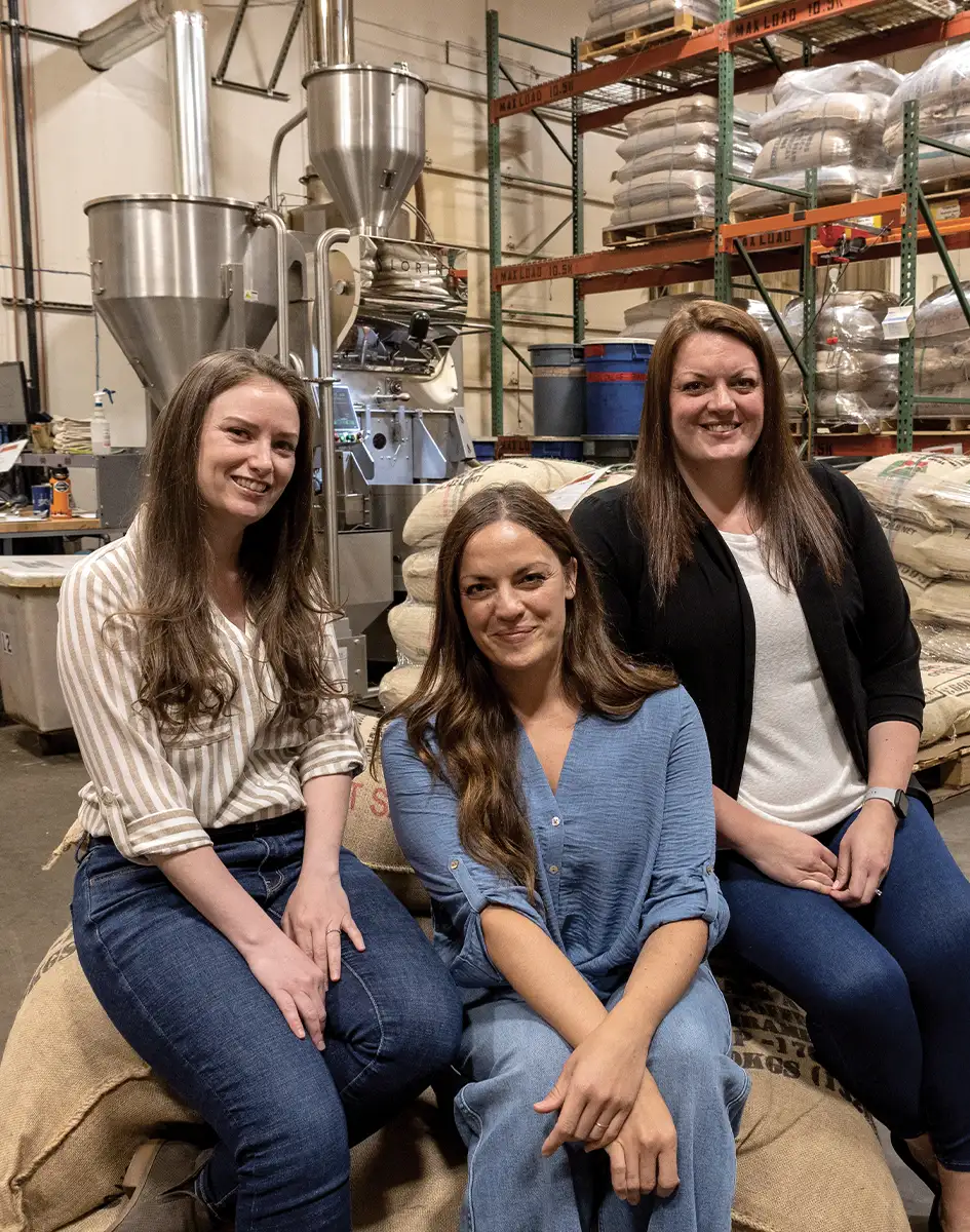 Michele Parkhurst (center), and VPs Julia Kelly (left) and Kori Wright (right) take a group photo in a Kaladi Brothers Coffee warehouse