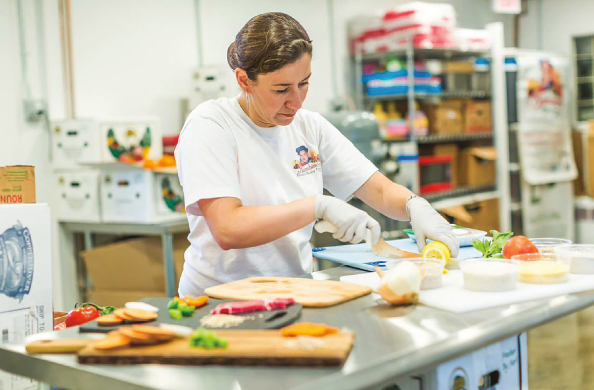 member of Bambino's Baby Food chopping vegetables and fruit in a kitchen