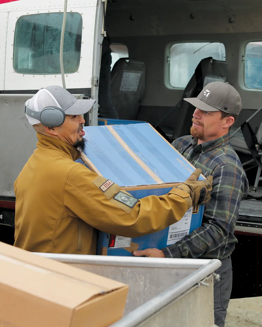 a man hands another man a carrier package from a plane