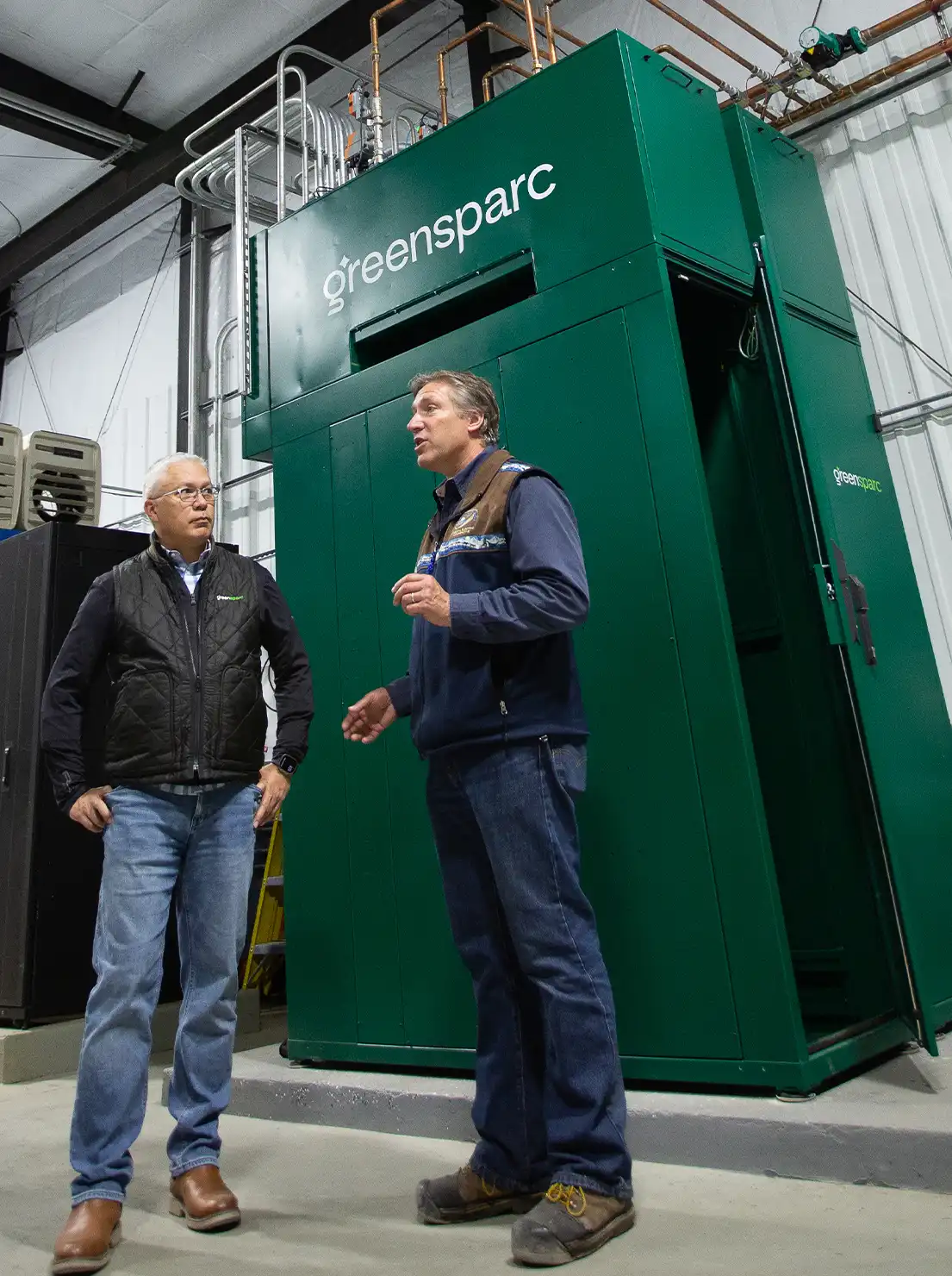 two men stand beside a GreenSparc cabinet in a large facility