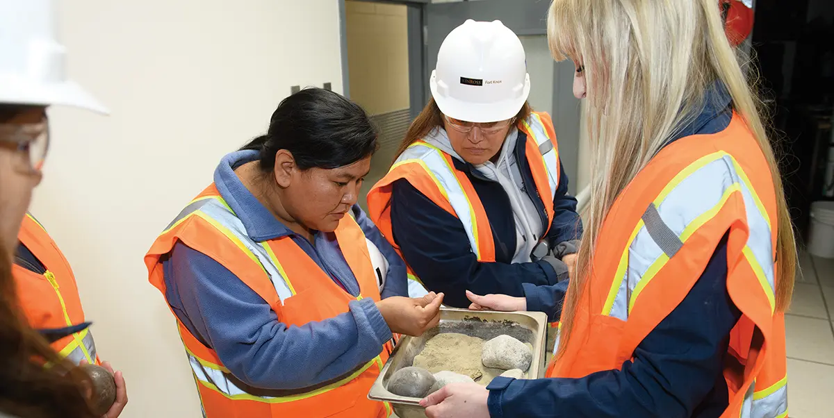 four women wearing safety vests and observing rocks in a tray