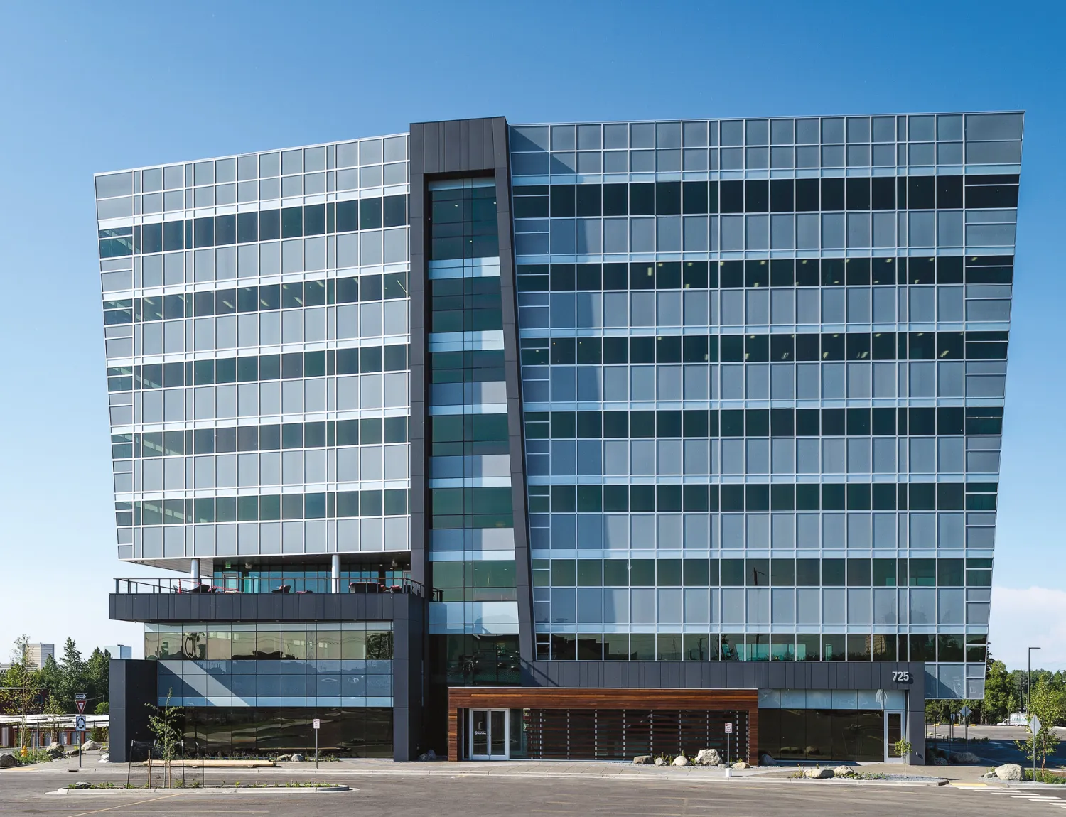 A modern, glass-fronted building with multiple stories and an asymmetrical design stands against a clear blue sky.