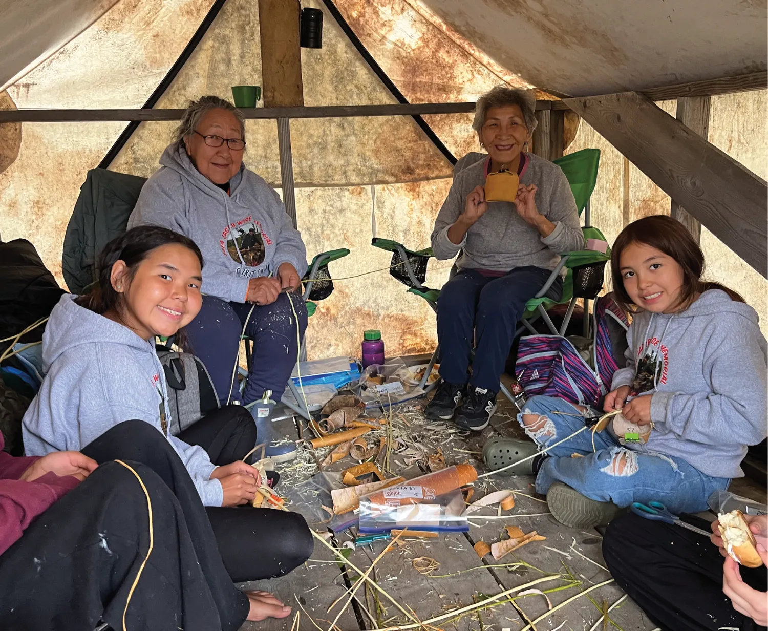 A multigenerational family sitting together inside a cozy tent, engaging in traditional crafting activities with smiles.