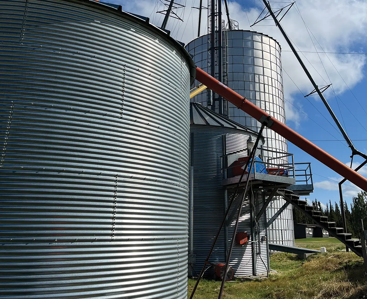 Portrait photograph of co-op galvanized bins all linked up by metal steel rusty structure shapes plus there's small staircase steps that lead up to one of the smaller co-op galvanized bin openings