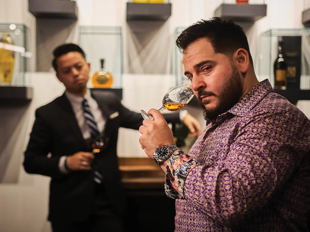 Ylli Ferati noses a whiskey in the foreground as Long Lam looks on from the background, holding a glass of his own