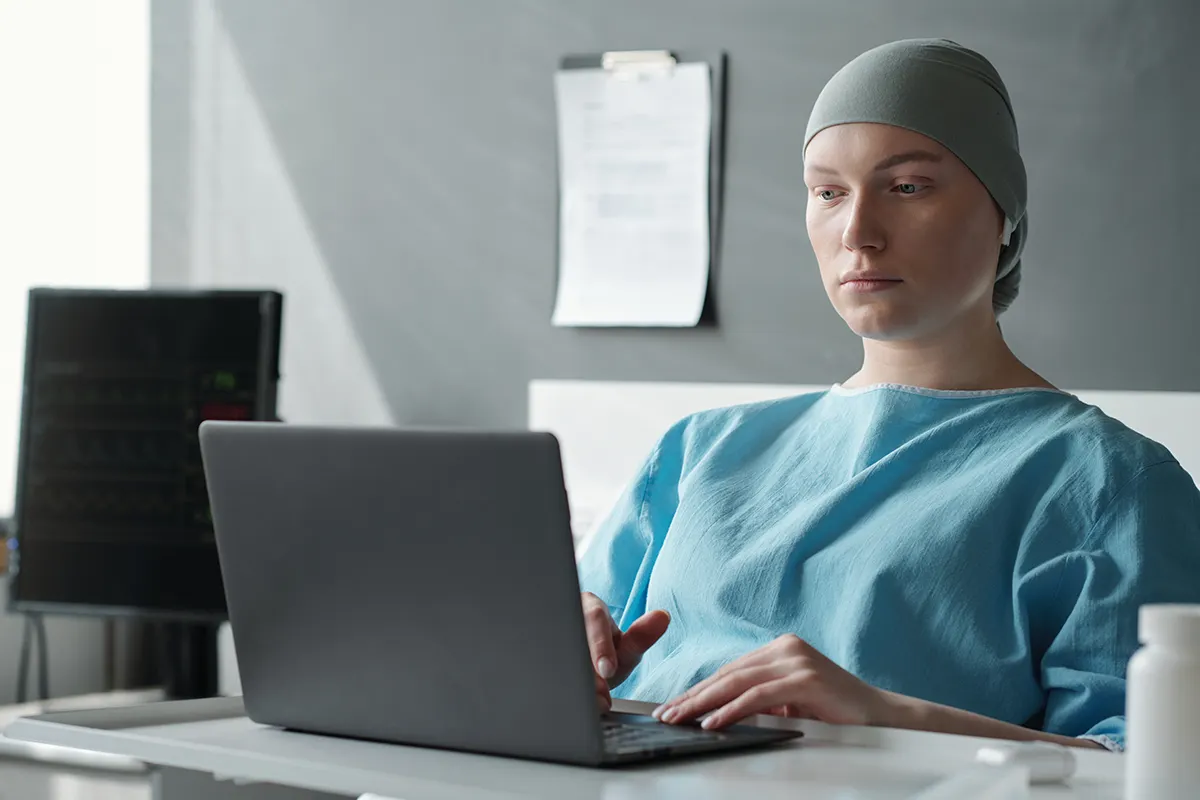 female cancer patient wearing a bandana browsing on a laptop while in a hospital bed