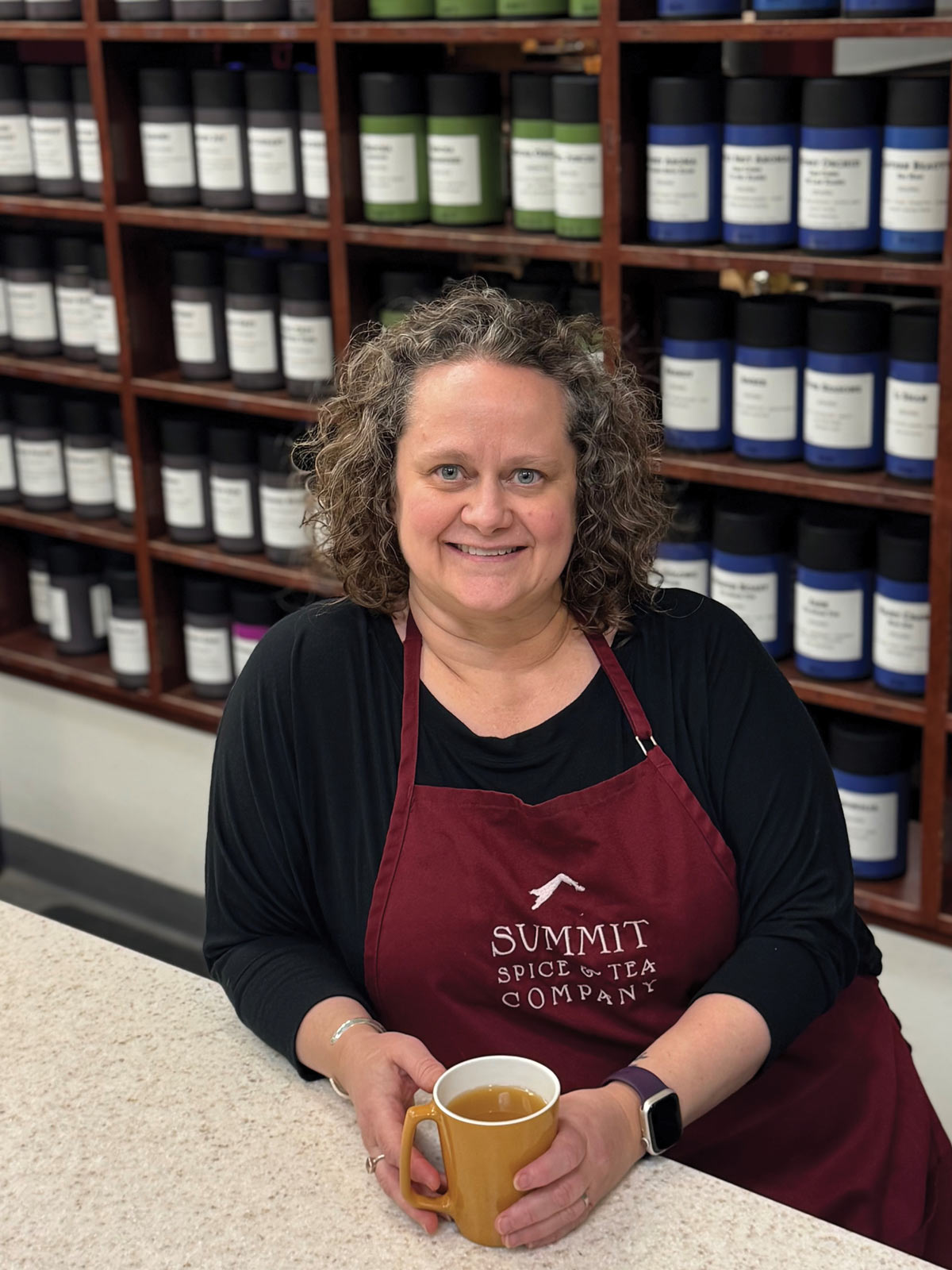 DeeAnn Apgar smiling while leaning against a counter with a mug in her hands