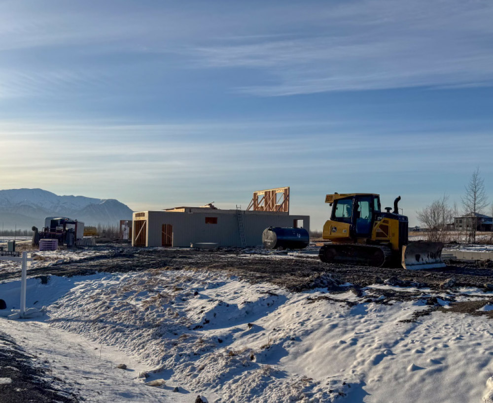 Construction site with a partially built building, snow on the ground, and a yellow bulldozer