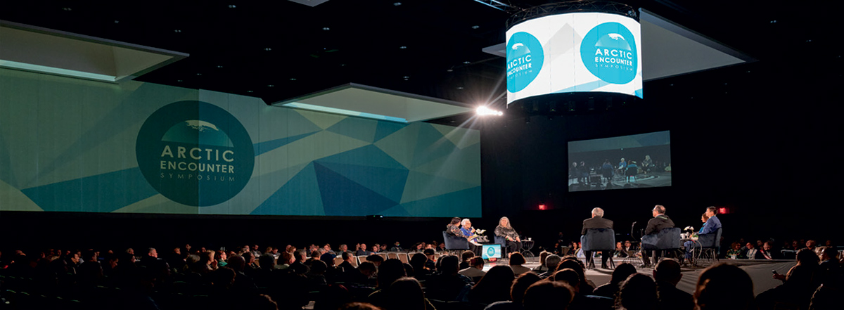 Arctic Encounter conference room with speakers on stage and logo projected on walls