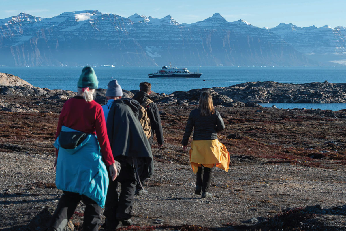 passengers walking towards rocky peninsula with boat cruise ship far out into the water