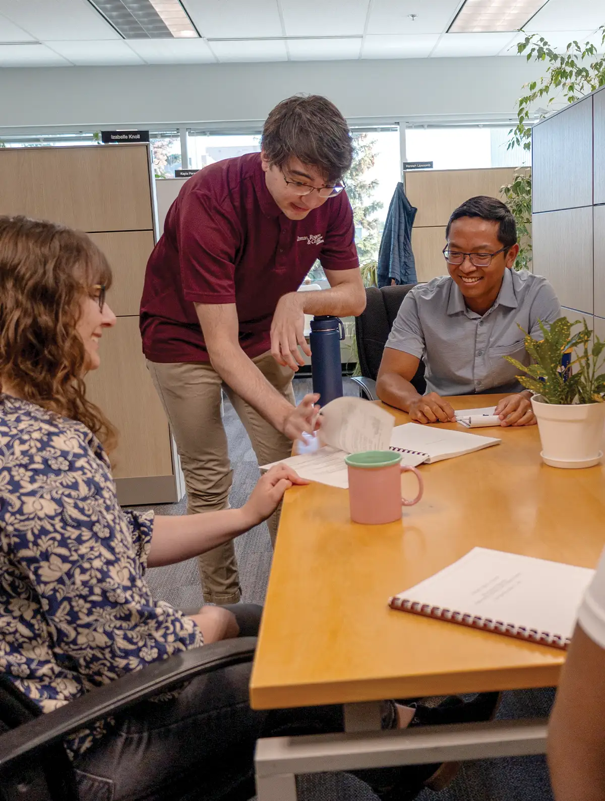 four office employees sit together at a table in a cubicle smiling while in discussion