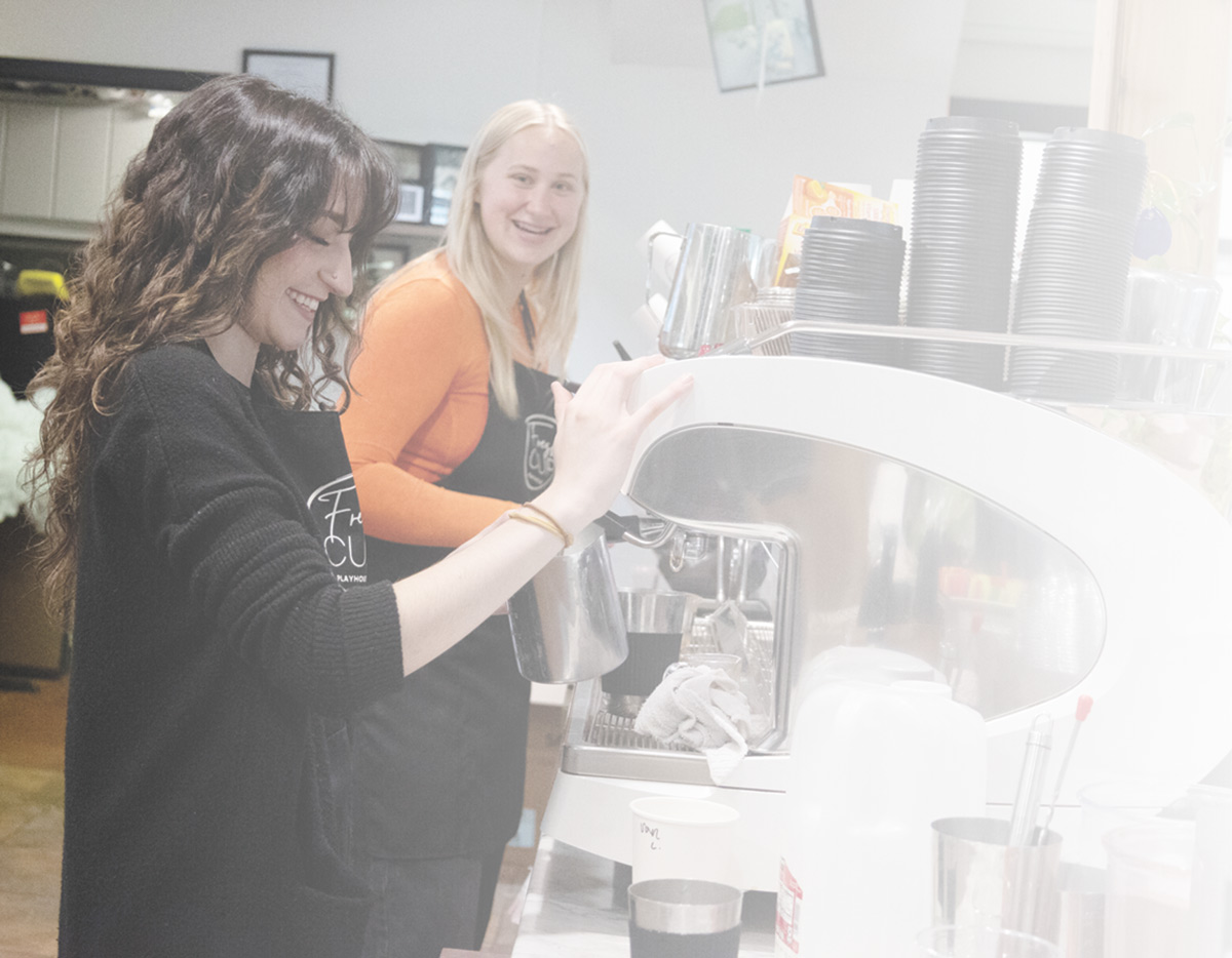 Two people working with a large white espresso machine in a cafe setting.